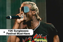 Performer in futuristic Y2K sunglasses singing into a microphone at a festival.