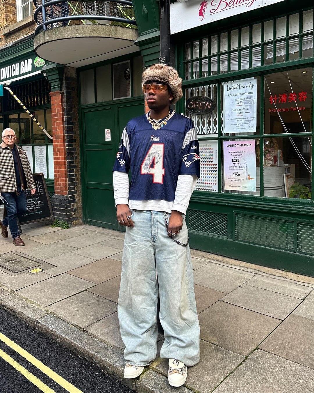 Man wearing oversized Patriots jersey and fur hat.