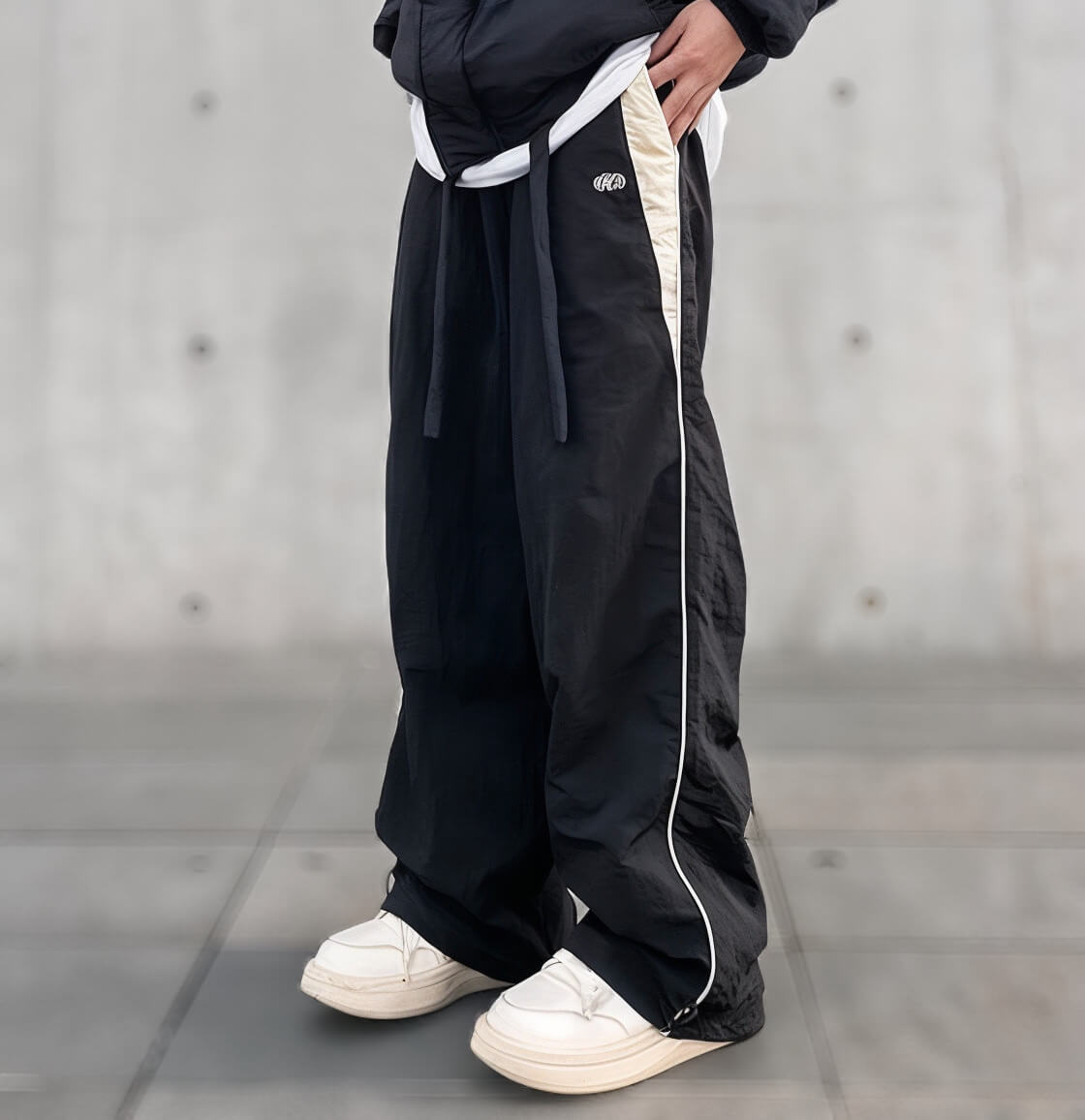 Black baggy pants with white stripe details, paired with white sneakers