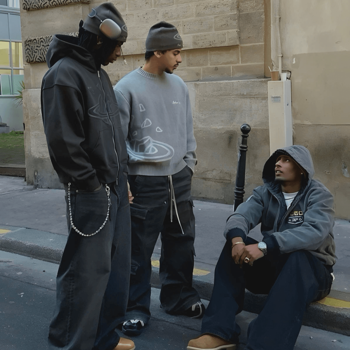 Three men in Y2K streetwear, standing and sitting by a stone building