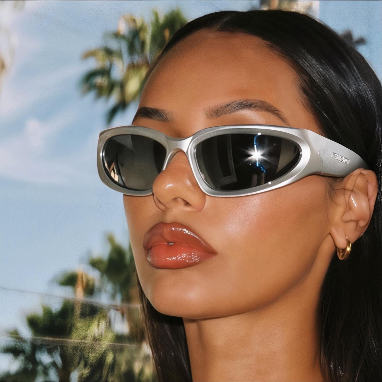 Woman in silver wrap-around sunglasses with palm trees reflected in lenses, Y2K