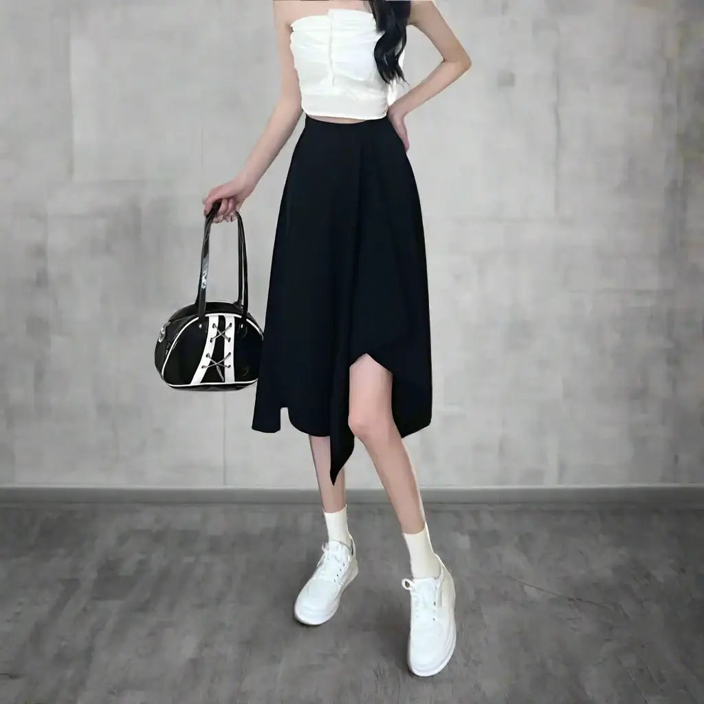 Woman in white crop top and asymmetrical wrap skirt holding a black handbag