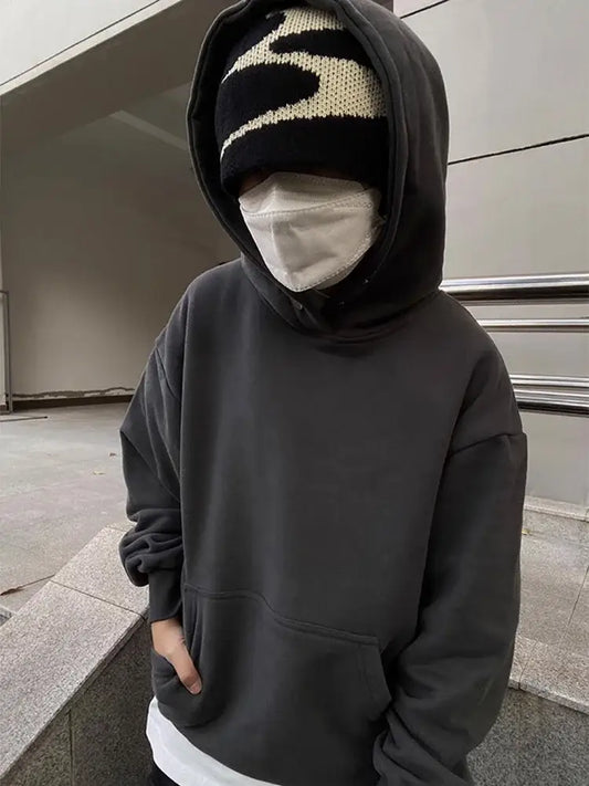 Hooded figure in a black sweatshirt and beanie showcasing Y2K accessories with a face covering