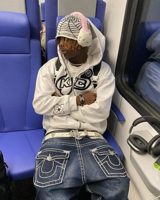 Person in a white Cyber Y2K Hoodie and baseball cap sitting on a blue seat