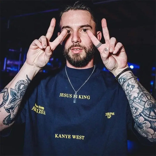 Bearded man in navy blue Kanye West T Shirt making peace signs with tattoos