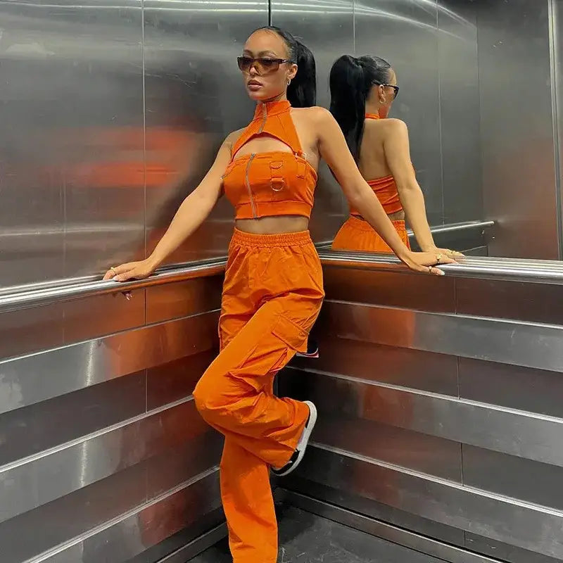 Woman stylishly poses in an elevator wearing vibrant orange cargo pants outfit