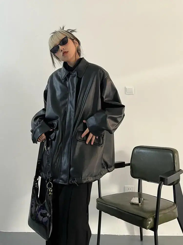 Person wearing an oversized leather jacket with short blonde hair and sunglasses