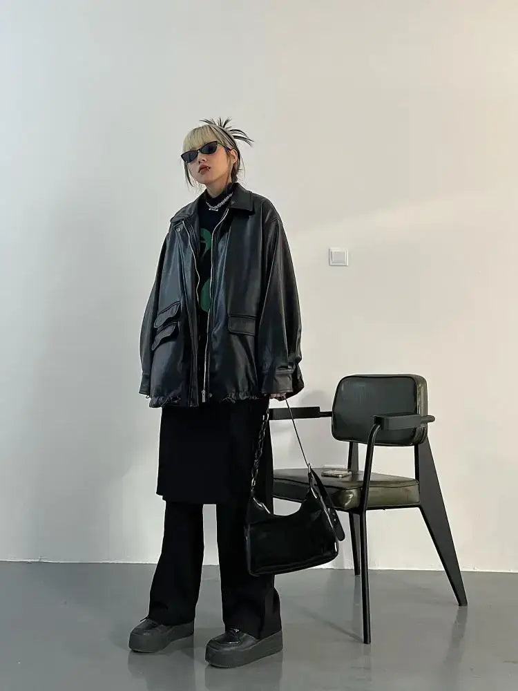 Person in oversized leather jacket and sunglasses standing next to a chair