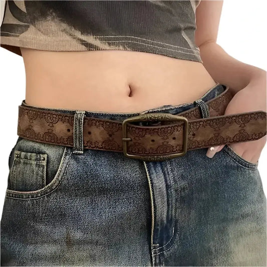 Decorative brown leather retro belt with embossed patterns over blue jeans and retro belt buckle