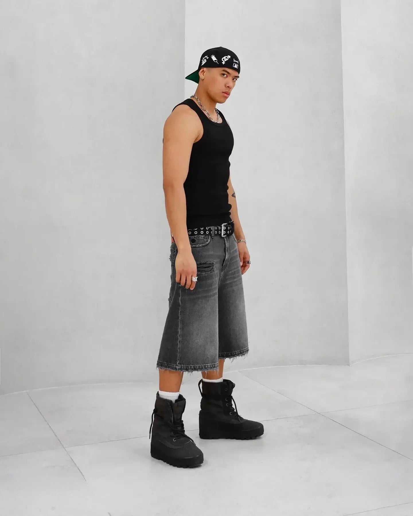 Person in a black tank top and gray ripped jean shorts with black boots and a bandana