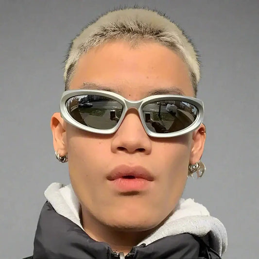 Person wearing sporty silver sunglasses with ear piercings showcasing Y2K streetwear style