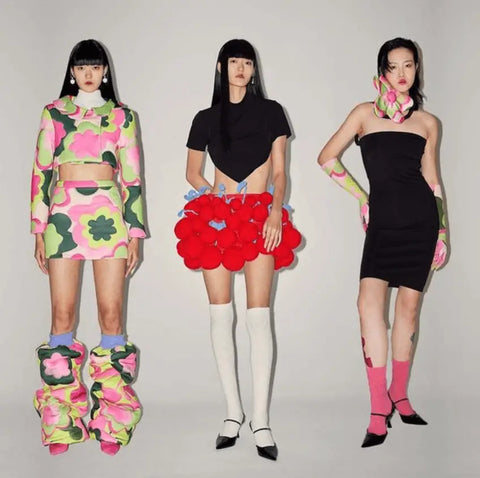 Three women in bold floral and geometric Y2K fashion outfits at a fashion show.