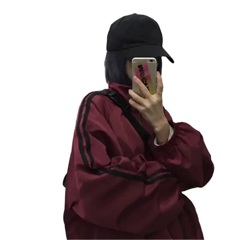 Person in a black baseball cap and maroon tracksuit jacket taking a selfie