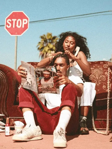 Two friends enjoying Y2K fashion outdoors, one elegantly braiding the other’s hair.