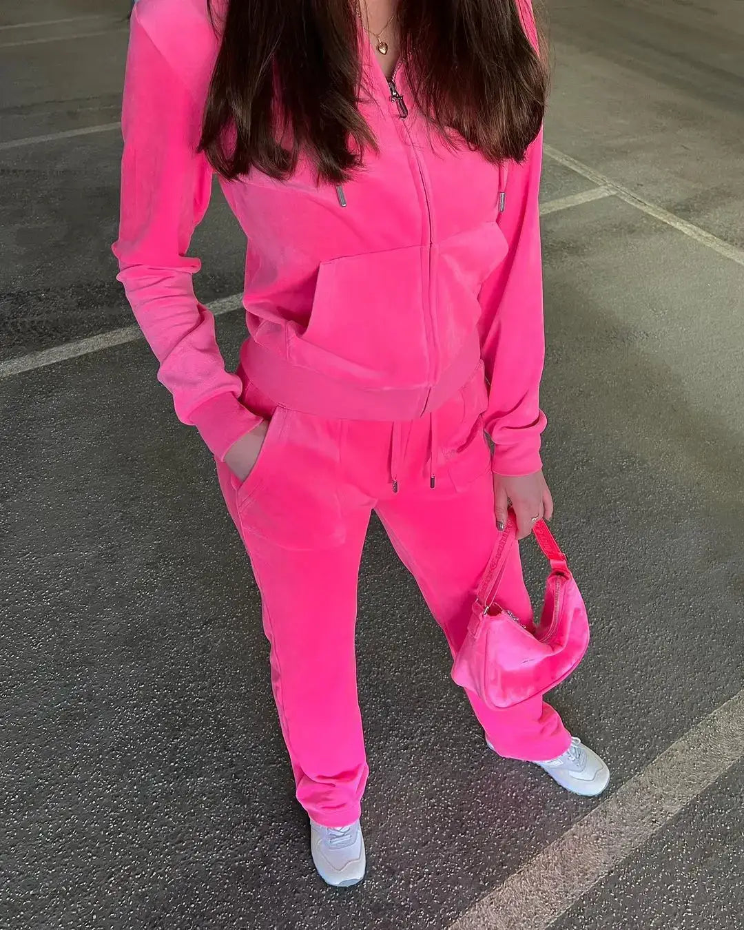 Person in bright pink tracksuit showcasing stylish velour sweat outfits on pavement