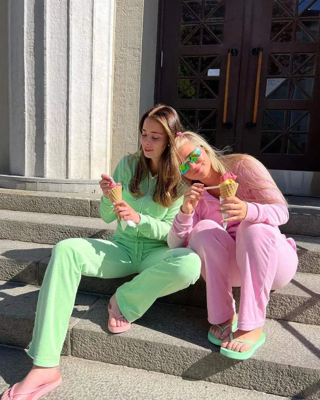 Two young women in colorful velour sweat outfits enjoying ice cream on stone steps