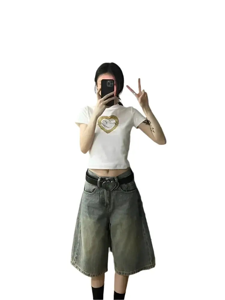 Person in white crop top and olive green shorts taking a selfie with washed black denim