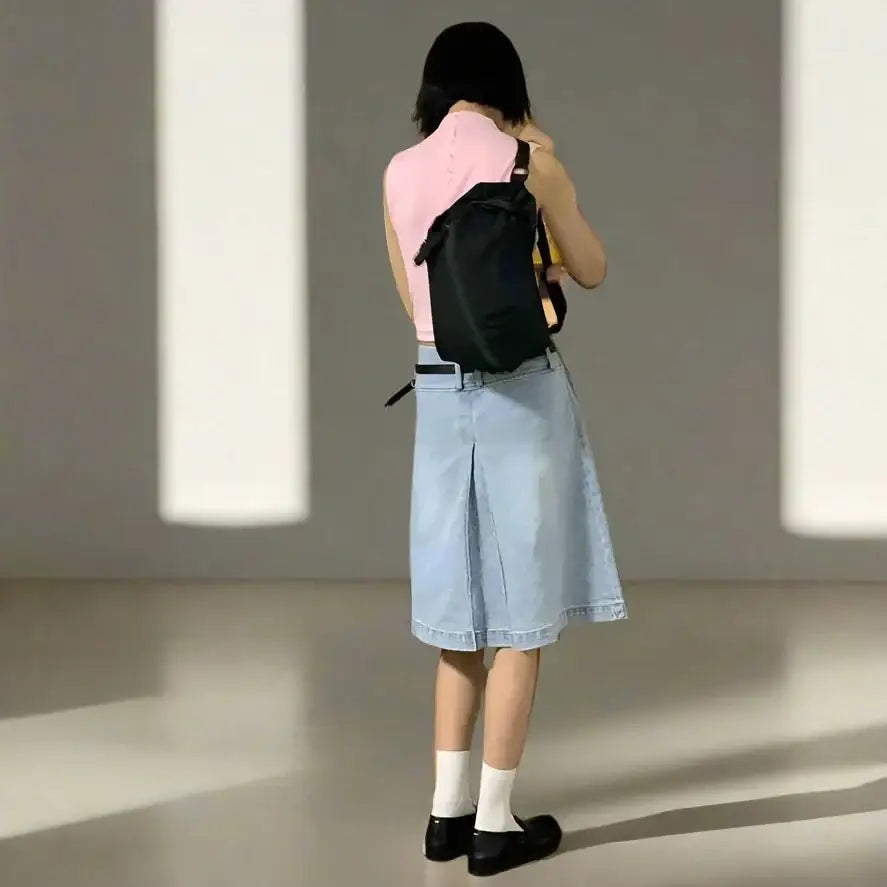 Person in pink top and light blue Y2K denim skirt with a black backpack