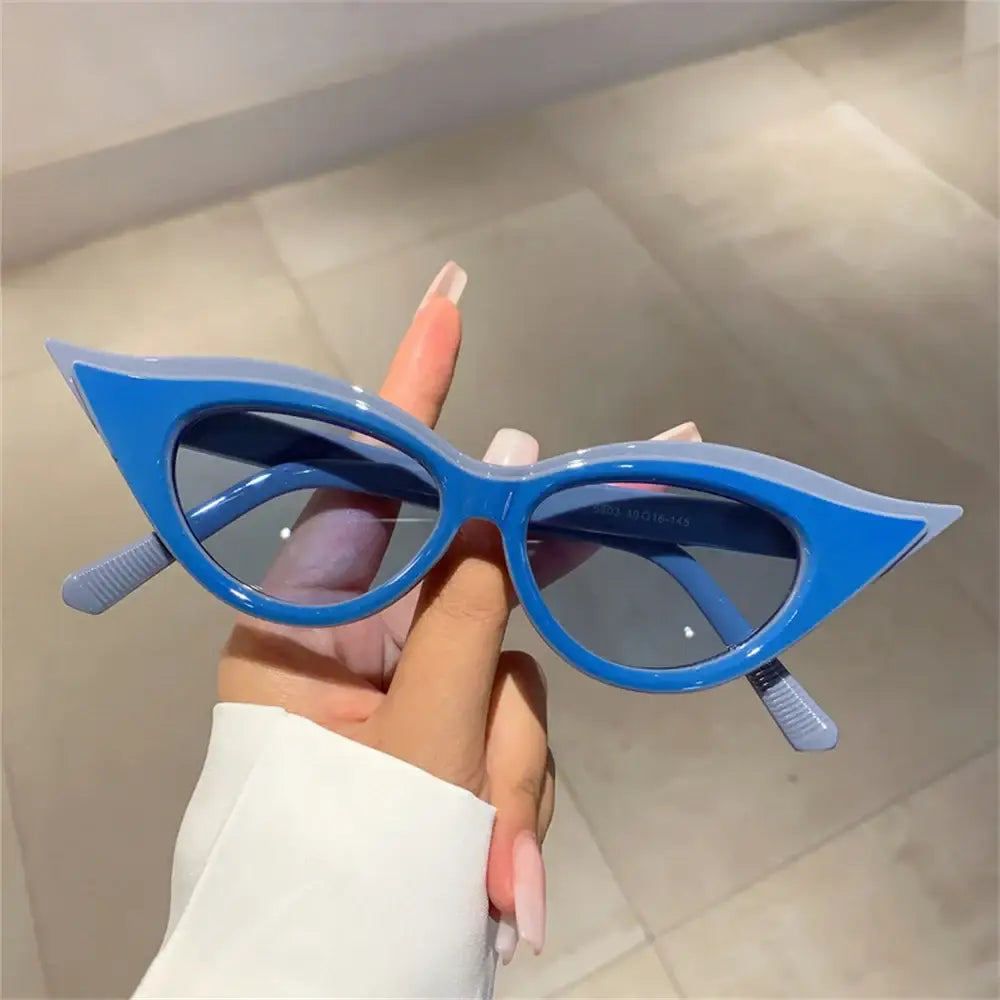 Bright blue cat-eye sunglasses for Y2K fashion held by a hand with painted nails