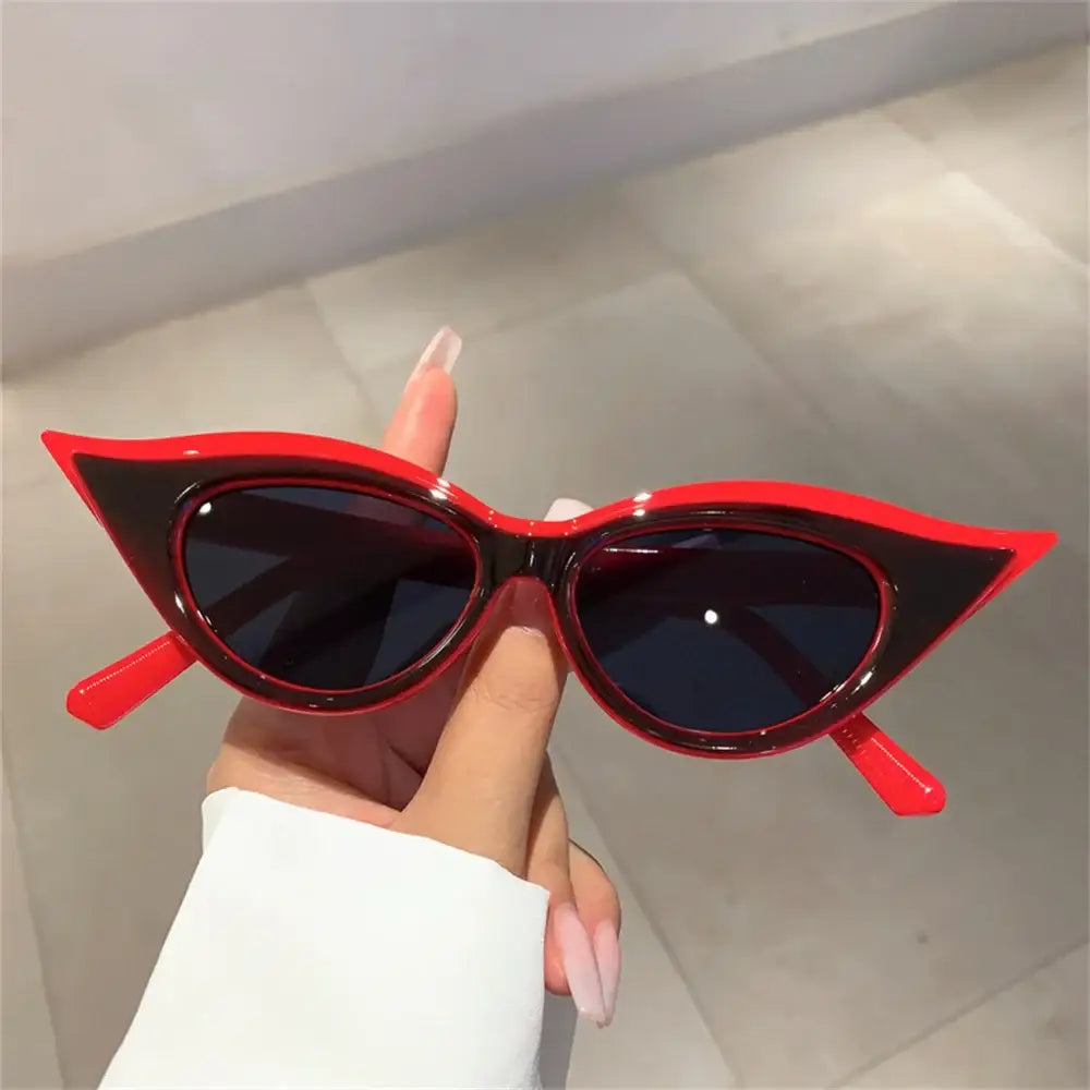 Red cat-eye Y2K fashion sunglasses with dark lenses held in a hand