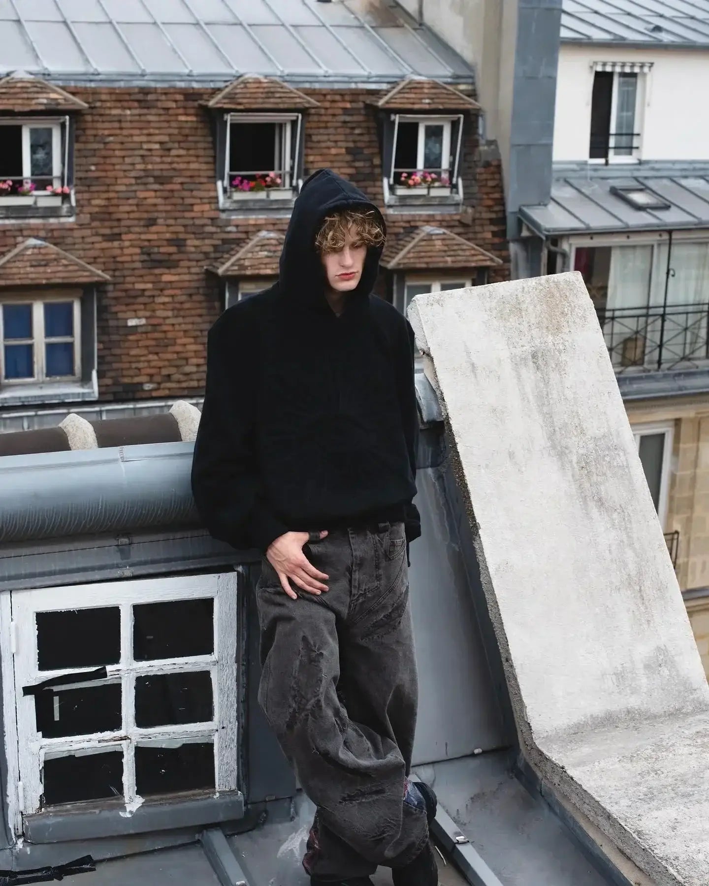 Person in a black Y2K hoodie design and jeans stands stylishly on a rooftop