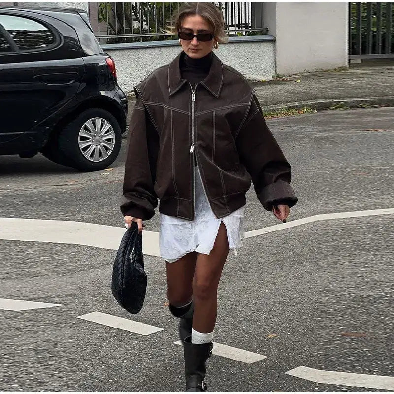 Woman in oversized brown Y2K leather jacket, white dress, and knee-high boots